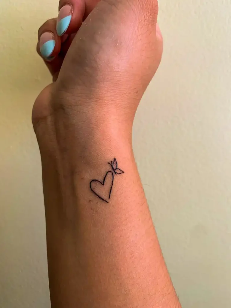 Minimalist heart and butterfly tattoo on a wrist.