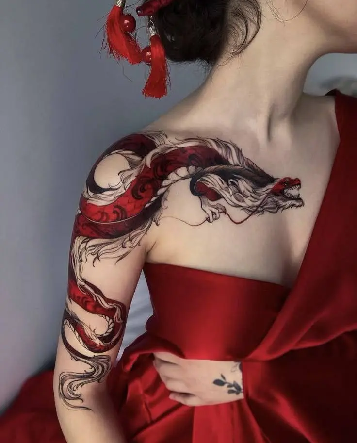 Red and black dragon tattoo on a woman's shoulder and arm.