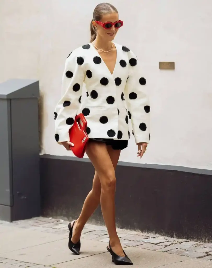 Fashion-forward street style featuring a woman in a polka dot jacket, red sunglasses, and black heels.