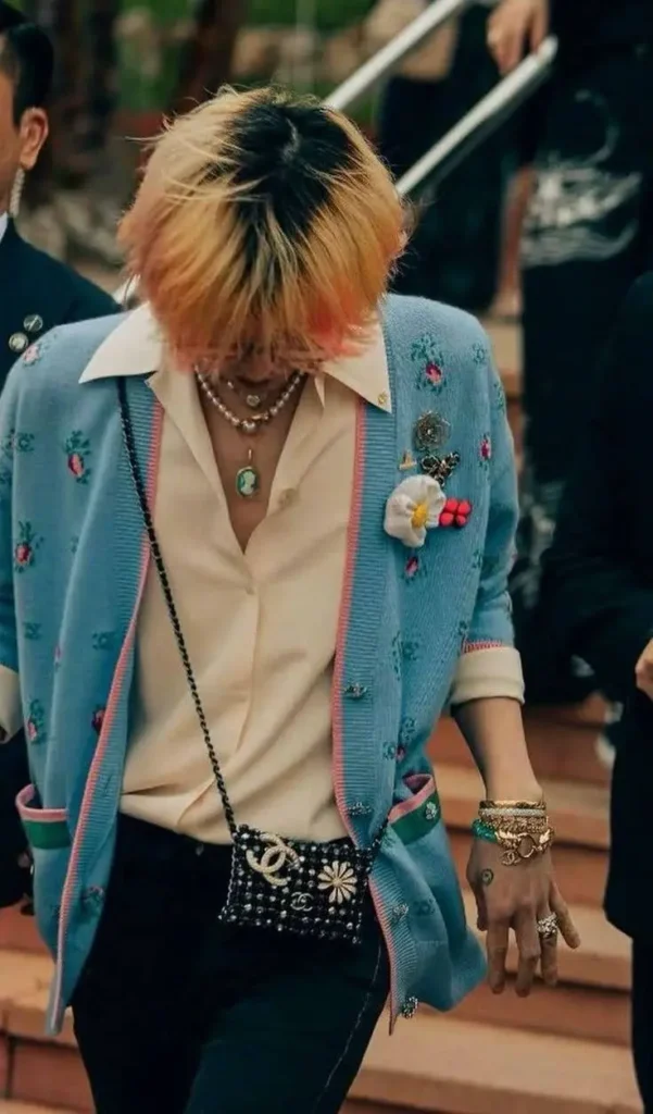 kpop singer wearing a trendy dress and jewelry , he is looking down and wearing a stylish bag.