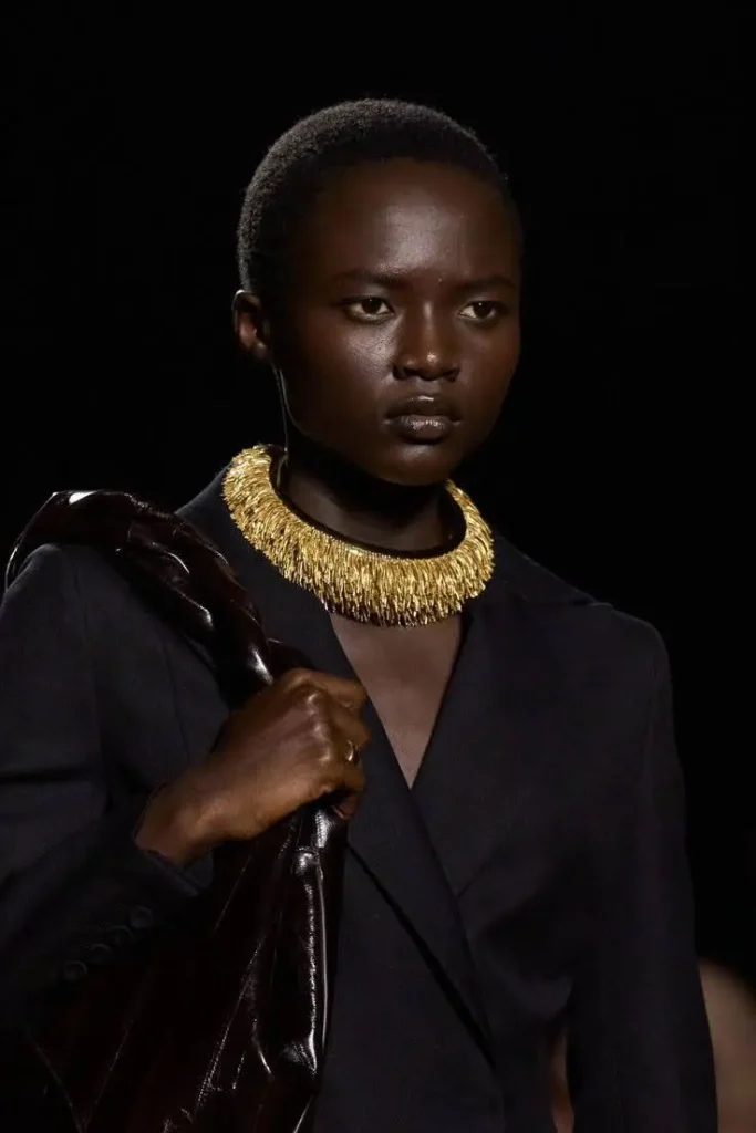 A runway female model wearing a gold sculptural necklace.