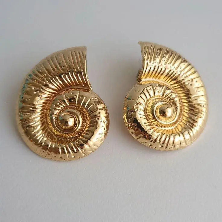 A gold sculptural earring pair on a flat surface.