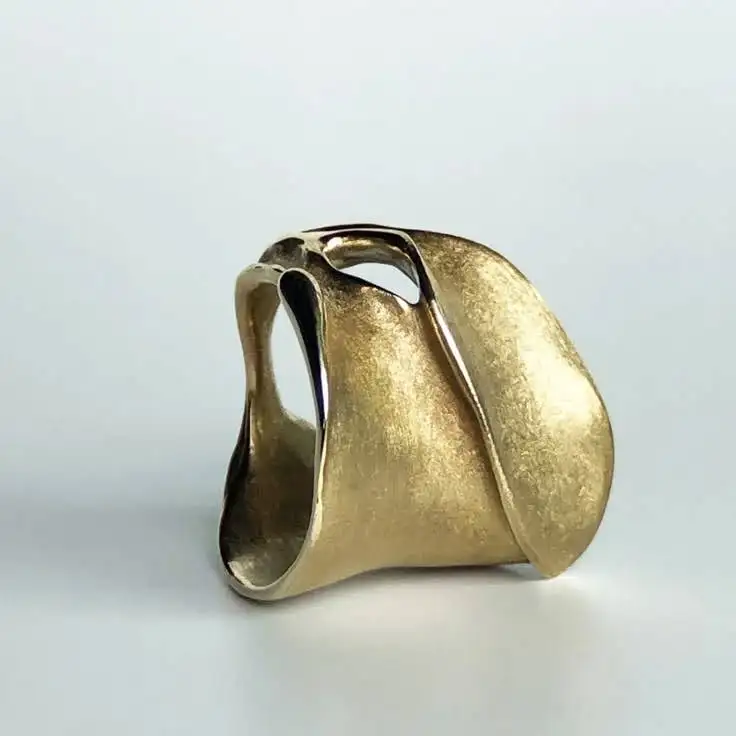 A gold sculptural ring on surface.