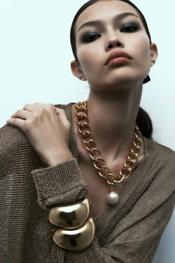 A woman showing a bold sculptural gold neckless and cuffs.