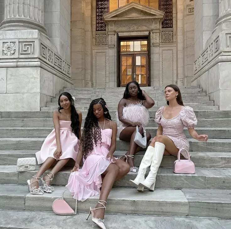 Four girls on steps in different pink outfits, showcasing various fashion aesthetics.