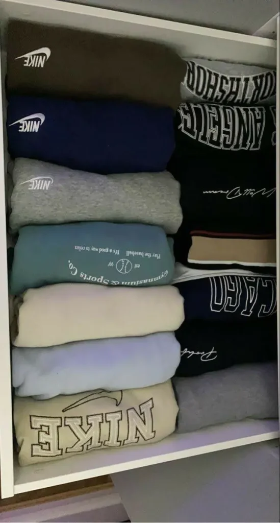 A white drawer filled with two vertical rows of neatly folded hoodies.