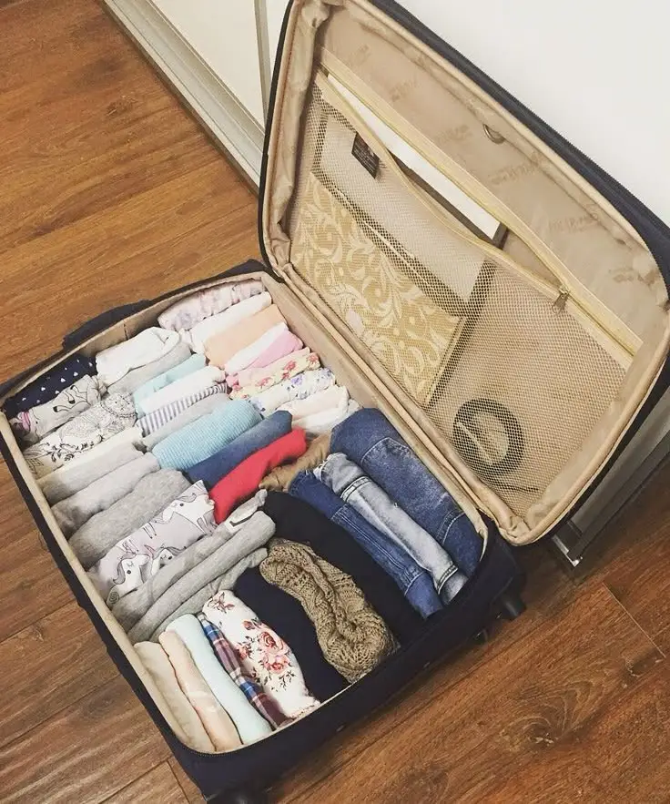 A blue suitcase with the lid open is packed with two rows of neatly rolled clothes for travel.