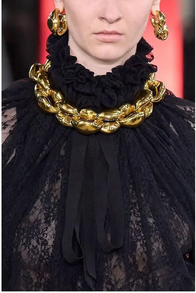 A runway model wearing a sculptural gold necklace and earrings.