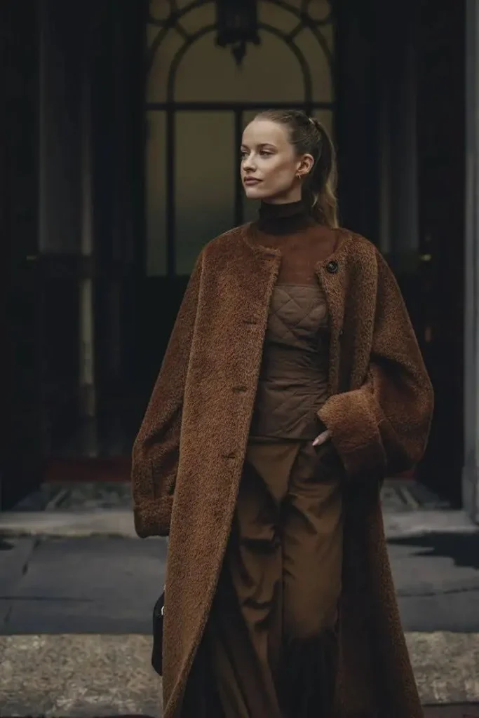 A woman wearing a monochromatic outfit of brown trousers, a quilted bustier, and a textured coat.