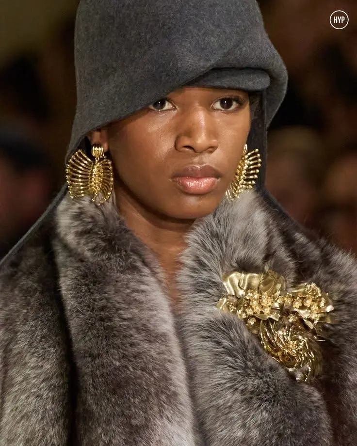 A runway female model wearing brooches on her fur coat.