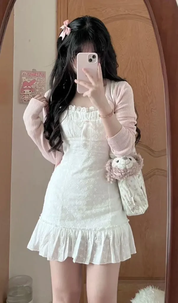 A young woman in a sweet, feminine pink cardigan and white dress, embodying the soft girl aesthetic.