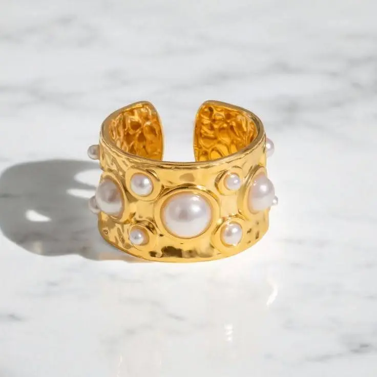 A modern gold pearl ring lying on a flat surface.