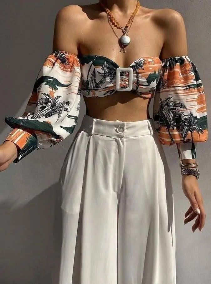 A woman wears a vintage-inspired outfit with a tropical-print off-the-shoulder crop top and high-waisted white pants.
