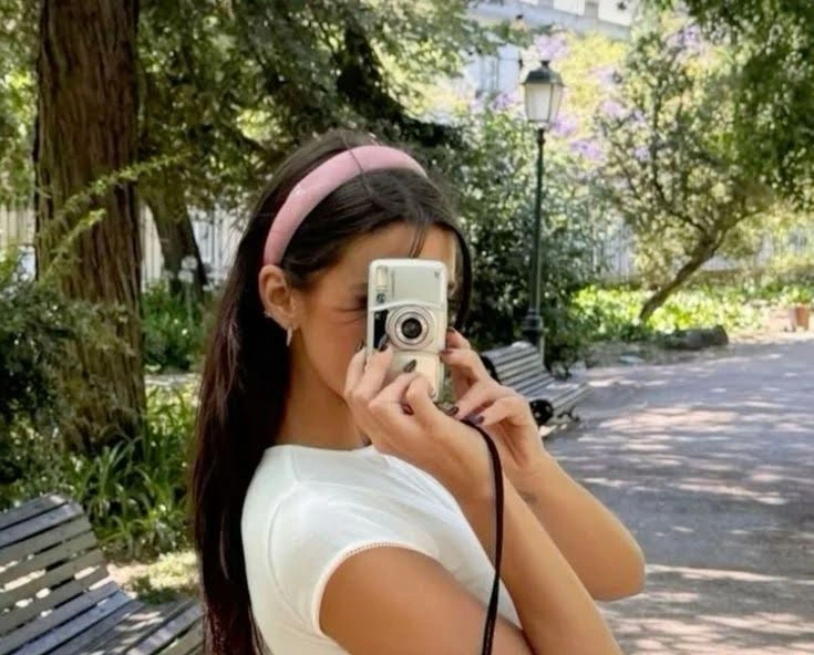 Girl in pink headband photographing outdoors, embodying a popular aesthetic.