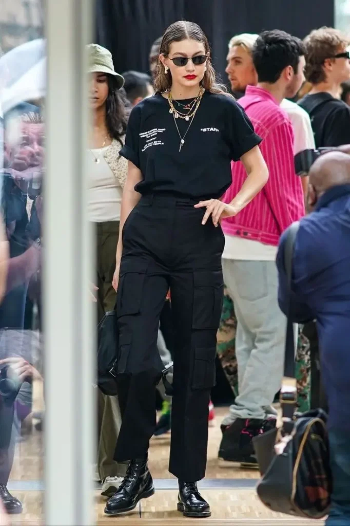 A fashion model wearing a black t-shirt and high-waisted black cargo pants with shiny boots.