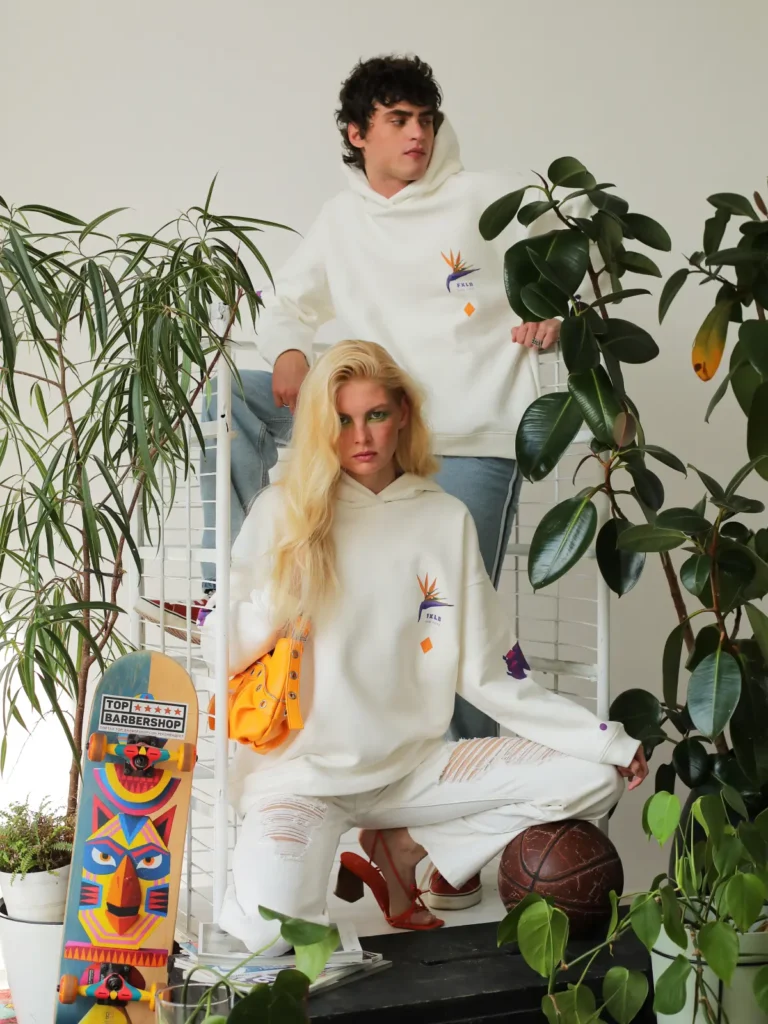 A couple wearing matching white hoodies and jeans pose on a metal staircase among plants.