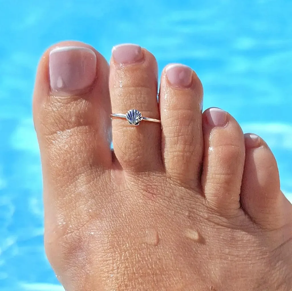A woman wearing silver seashell ring on toe.