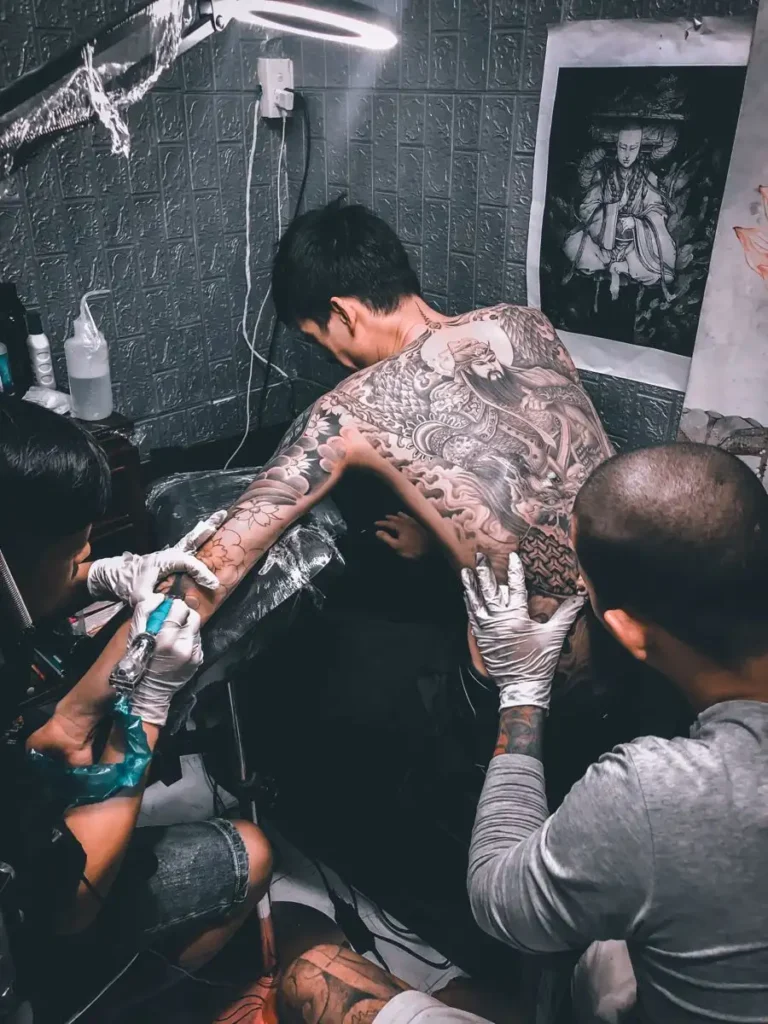 A girl is making tattoo on a guy back.