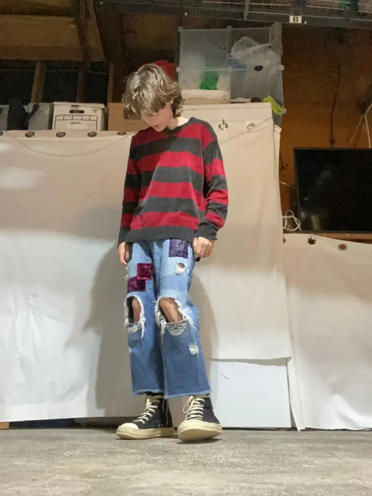 a boy wearing stylish ripped jean and shirt.