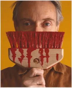Roy Lichtenstein with holding a brush with red color paint on it infront of face