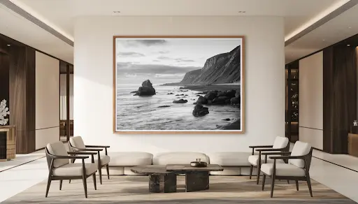 A luxurious interior space features a large, framed black and white coastal photograph on a pristine white wall, complemented by refined modern furniture in neutral tones with natural and dark wood accents, under soft, warm lighting that creates an inviting and aspirational atmosphere, embodying quality craftsmanship and appealing to stylish homeowners and interior designers in the USA.