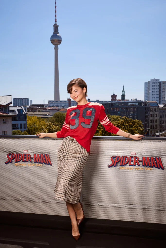 Zendya wearing wearing a red Coach football jersey tucked into a beige plaid midi skirt